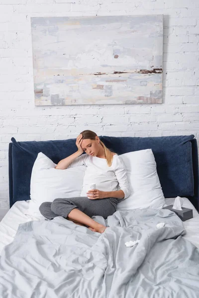 Selektiver Fokus kranker Schwangerer mit Tasse in der Nähe von Servietten auf dem heimischen Bett — Stockfoto