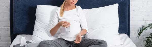 Imagen horizontal de la mujer embarazada sosteniendo un vaso de agua y pastillas en la cama - foto de stock