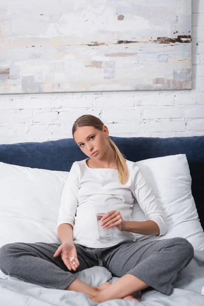 Concentration sélective de la jeune femme enceinte tenant des pilules et un verre d'eau dans la chambre — Photo de stock