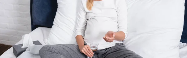 Заголовок сайта беременной женщины, держащей стакан воды возле коробки с салфетками на кровати — стоковое фото