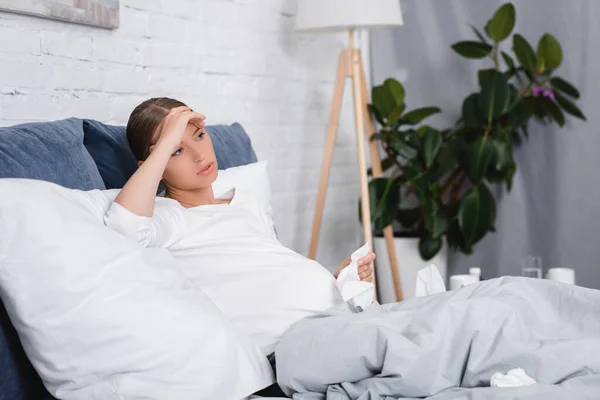 Selective focus of diseased pregnant woman holding napkin on bed — Stock Photo
