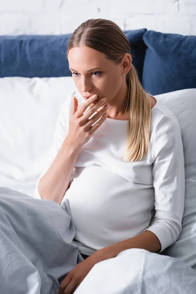 Concentration sélective de la femme enceinte touchant la bouche sur le lit — Photo de stock