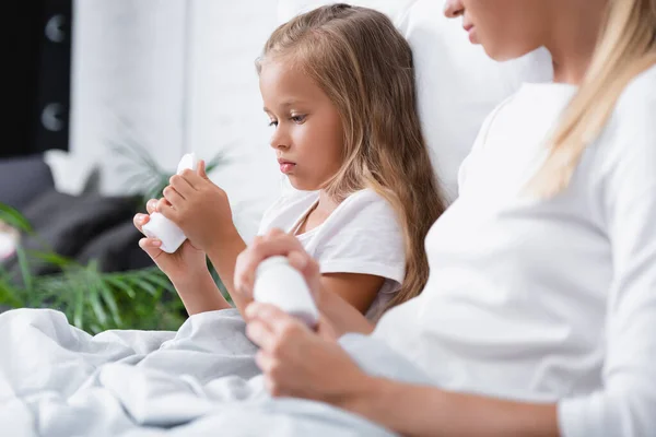 Focus selettivo del bambino guardando vaso con pillole vicino alla madre sul letto — Foto stock