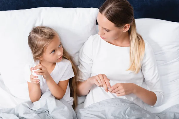 Woman looking at child while holding jar with pills on bed — Stock Photo