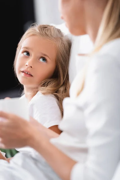 Selective focus of child looking at mother with cup on bed — Stock Photo