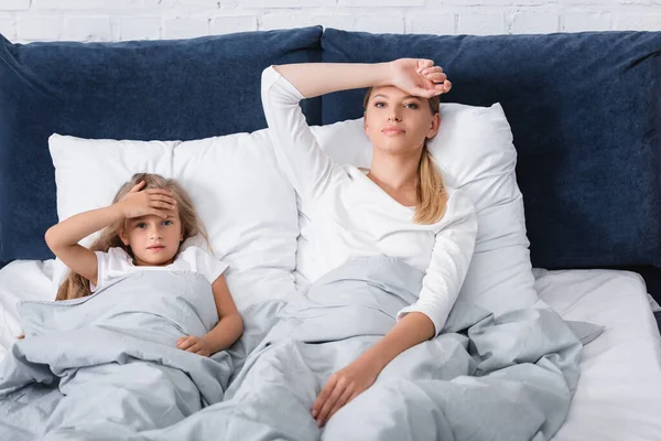 Concentration sélective de la mère malade regardant la caméra près de l'enfant sur le lit — Photo de stock