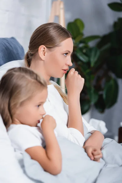 Selective focus of sick woman coughing near daughter on bed — Stock Photo