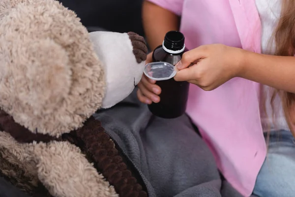 Selective focus of girl holding spoon and syrup near teddy bear — Stock Photo