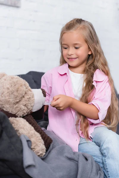 Foyer sélectif de l'enfant tenant cuillère de sirop près de peluche sur le canapé — Photo de stock