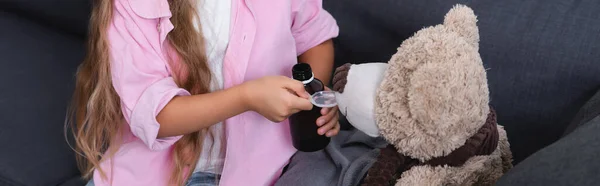 Panoramic crop of kid holding spoon and bottle of syrup near teddy bear — Stock Photo