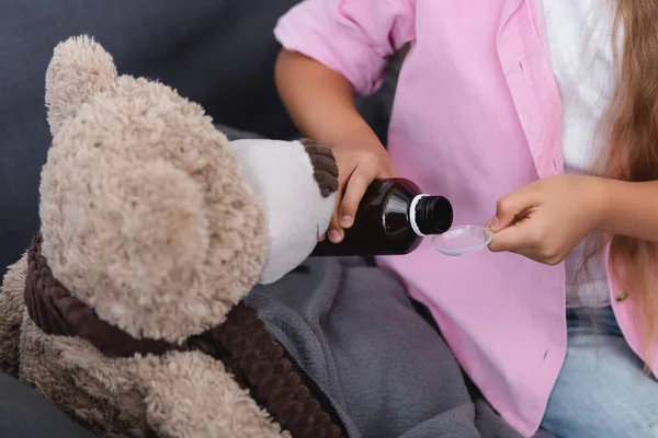 Ausgeschnittene Ansicht von Kind gießt Sirup in Löffel in der Nähe Teddybär zu Hause — Stockfoto