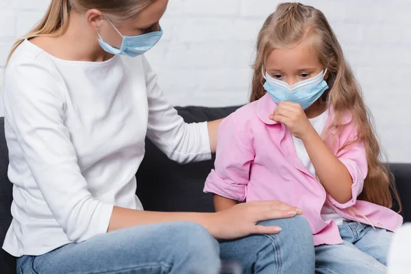 Selective focus of girl in medical mask sitting near mother on couch — Stock Photo
