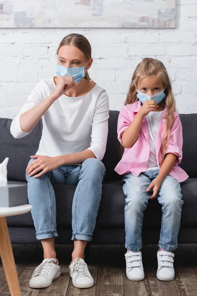 Selective focus of mother in kid in medical masks couching on couch — Stock Photo
