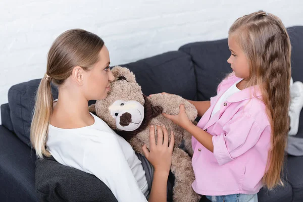 Hija dando suave juguete a enfermo madre en sofá - foto de stock