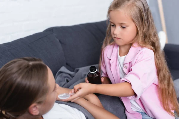 Concentration sélective de la femme couchée près de l'enfant avec une cuillère de sirop — Photo de stock