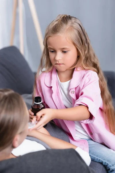 Concentration sélective de la fille donnant du sirop à la mère malade sur le canapé — Photo de stock