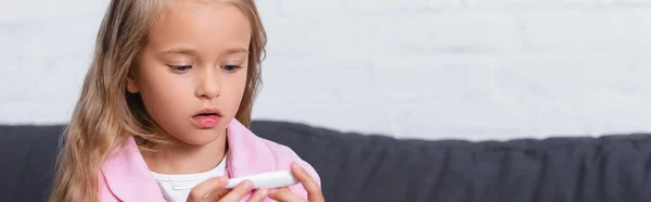 Panoramic shot of child looking at thermometer at home — Stock Photo
