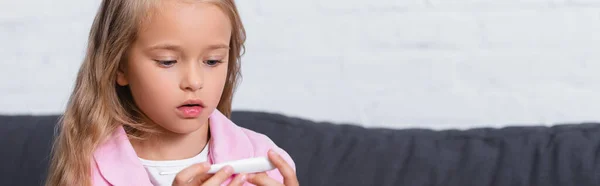 Plan panoramique d'un enfant regardant un thermomètre à la maison — Photo de stock