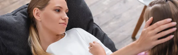 Заголовок сайта больной женщины, трогающей голову дочери на диване — стоковое фото