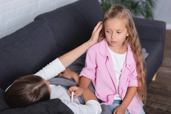 Selective focus of sick woman touching hair of daughter with thermometer at home — Stock Photo