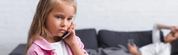 Foto panorámica del niño hablando en el teléfono inteligente cerca de la madre enferma en el sofá - foto de stock