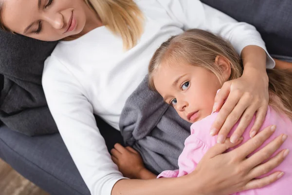 Vue du dessus de la femme malade embrassant l'enfant sur le canapé — Photo de stock