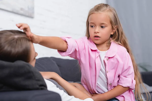 Selective focus of child touching forehead of sick mother on couch — Stock Photo