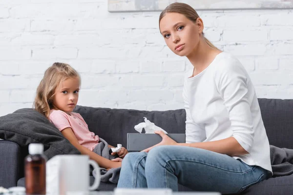 Selective focus of woman holding box with napkins beside ill daughter on couch — Stock Photo