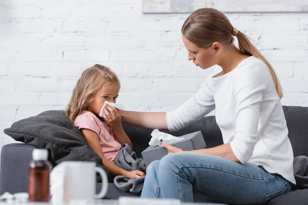 Selective focus of woman holding napkins near daughter with snuffle on couch — Stock Photo