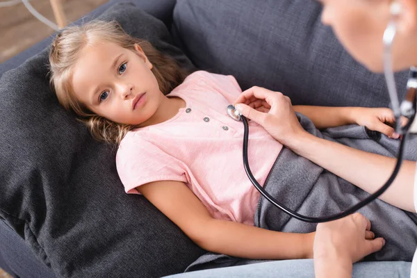 Selective focus of ill child holding hand of mother in stethoscope — Stock Photo