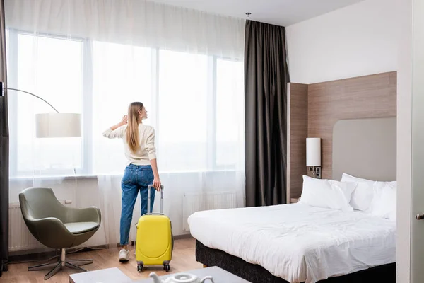 Mujer joven de pie con equipaje amarillo en la habitación de hotel - foto de stock