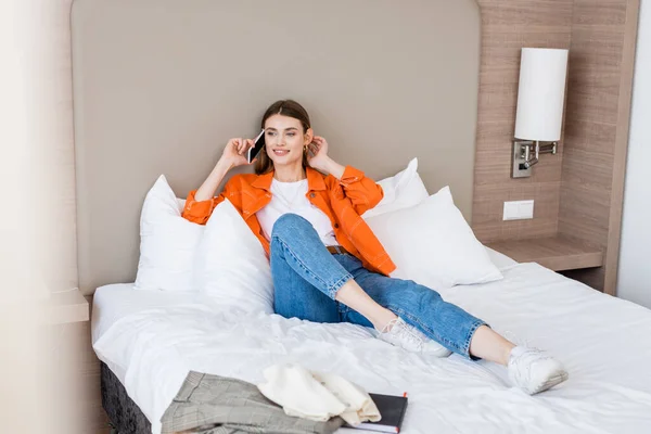 Jovem mulher falando no smartphone perto de roupas na cama — Fotografia de Stock