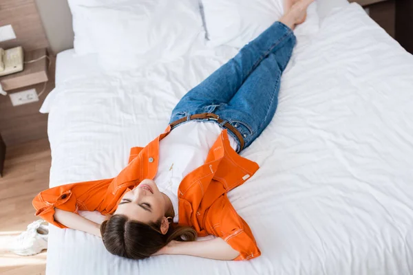 High angle view of young woman in denim jeans resting on bed in hotel — Stock Photo