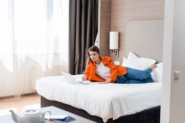 Enfoque selectivo del freelancer acostado en la cama y el uso de la computadora portátil en la habitación de hotel - foto de stock