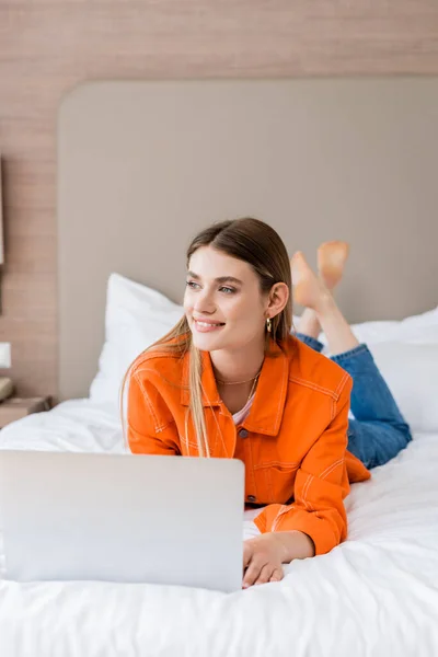 Barefoot freelancer lying on bed near laptop in hotel room — Stock Photo