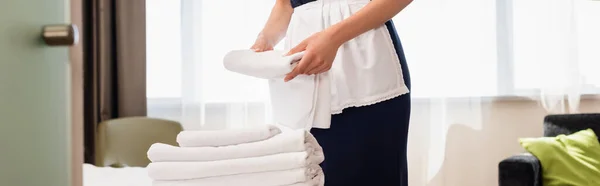 Cropped view of maid in apron holding clean towel in hotel room, panoramic shot — Stock Photo