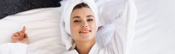 Vista dall'alto gioiosa donna in asciugamano e accappatoio bianco sdraiato sul letto in camera d'albergo, colpo panoramico — Foto stock