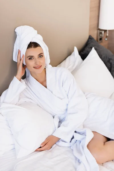 Giovane donna in asciugamano e accappatoio bianco sdraiata sul letto in camera d'albergo — Foto stock