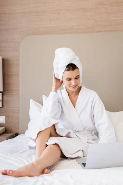 Young freelancer in bathrobe and towel looking at laptop on bed — Stock Photo