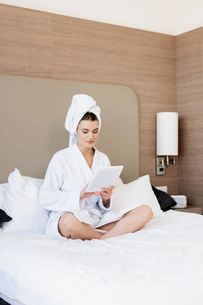 Mujer en toalla y albornoz blanco usando tableta digital en la habitación del hotel - foto de stock