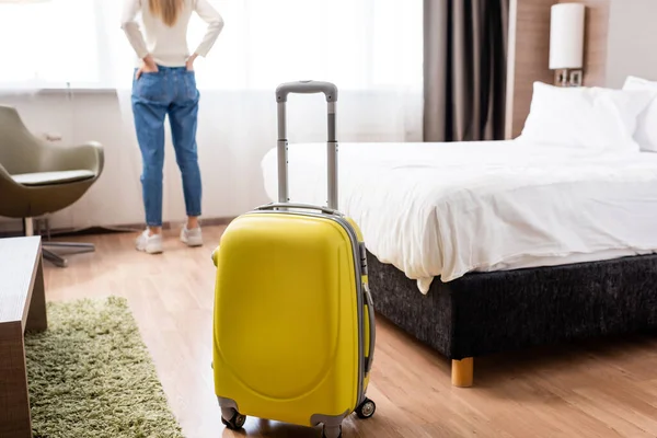 Селективное фокусирование желтого багажа рядом с женщиной в номере отеля — стоковое фото