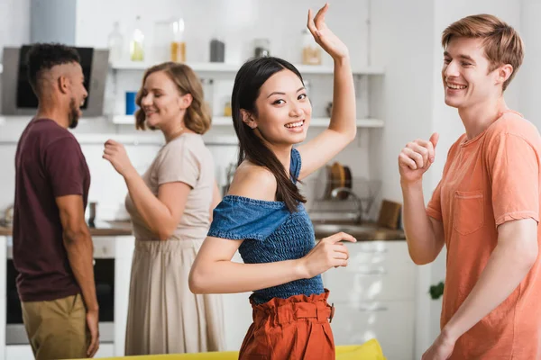 Alegre asiático mujer mirando cámara mientras bailando con multicultural amigos - foto de stock