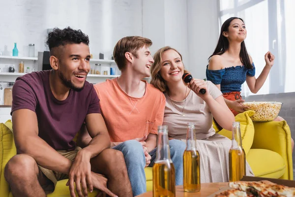 Enfoque selectivo de mujer asiática sosteniendo tazón de palomitas de maíz mientras amigos multiculturales cantando karaoke - foto de stock