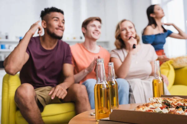 Enfoque selectivo de amigos multiétnicos cantando karaoke cerca de cerveza y pizza - foto de stock