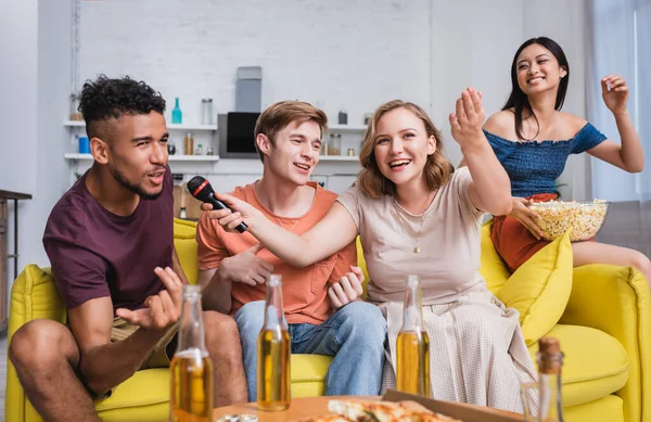 Excited multiethnic friends singing karaoke during party in kitchen — Stock Photo