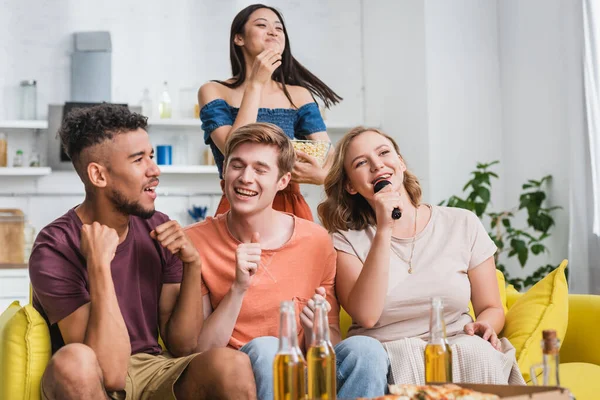 Joven mostrando el pulgar hacia arriba mientras canta karaoke con amigos multiculturales - foto de stock