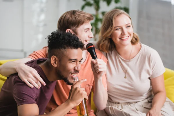 Selective focus of young man singing karaoke during party with multiethnic friends — Stock Photo