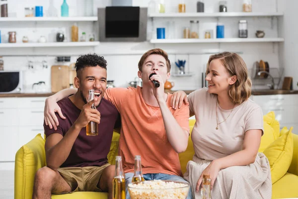 Joven cantando karaoke durante la fiesta con amigos multiétnicos - foto de stock