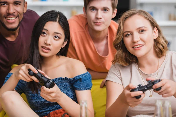 KYIV, UCRANIA - 28 de julio de 2020: enfoque selectivo de amigos multiétnicos concentrados jugando videojuegos durante la fiesta - foto de stock