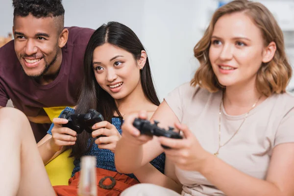KYIV, UCRANIA - 28 de julio de 2020: enfoque selectivo de amigos multiétnicos jugando videojuegos durante la fiesta - foto de stock
